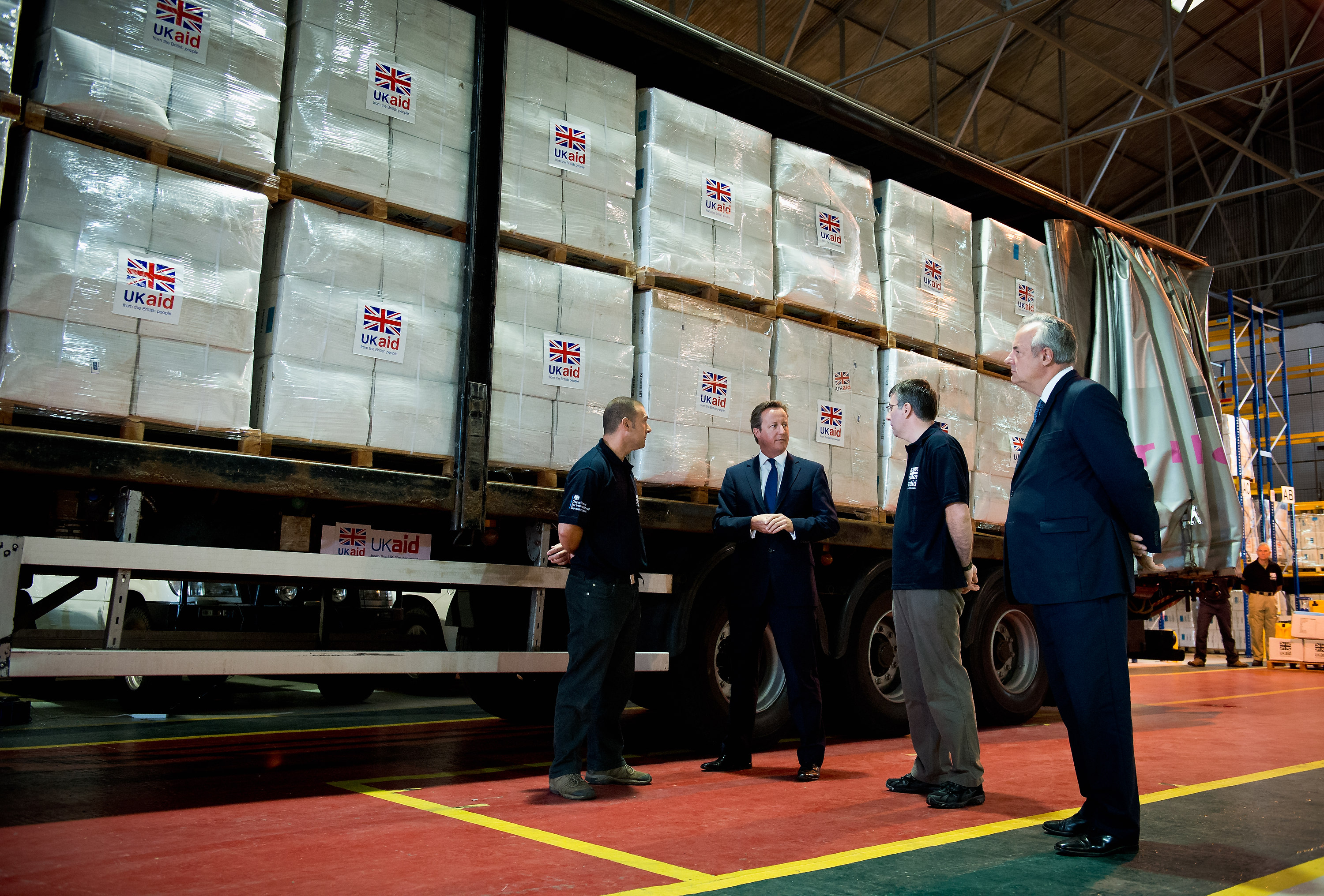 UK PM David Cameron visits a 'UK AID' facility in Wiltshire. He stands in a warehouse with boxes marked UK AID.